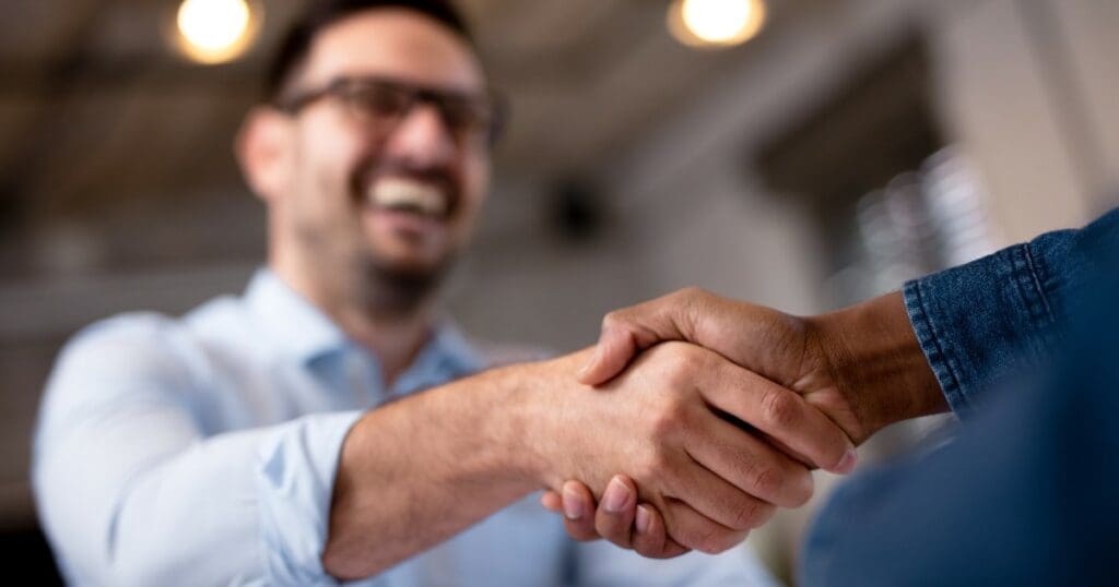 two people shaking hands with a man smiling