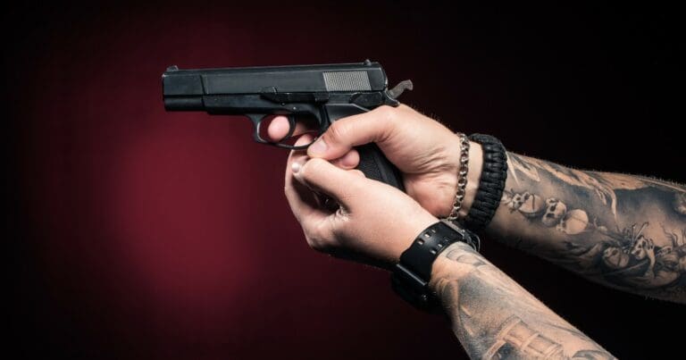 a close up photo of a person with tattoos holding a handgun with both hands