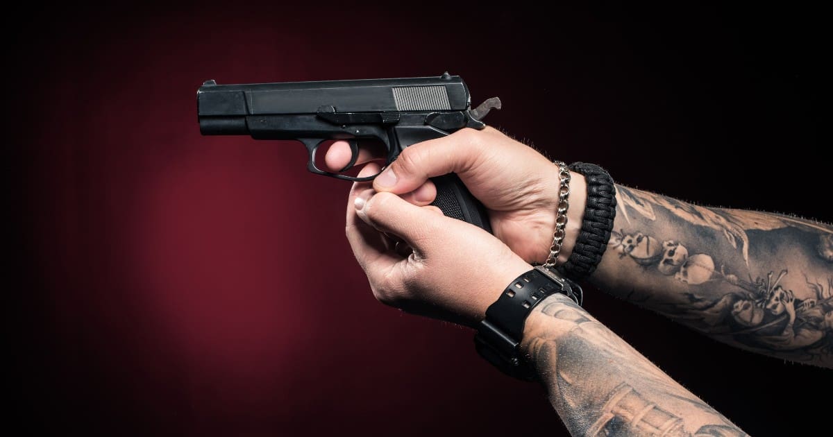 a close up photo of a person with tattoos holding a handgun with both hands